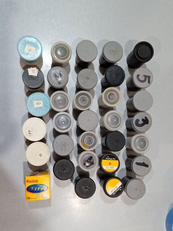 Кілька десятків касет і контейнерів фотоплівки 35 мм, зокрема Kodak і ProFoto, розкладені рядами на столі